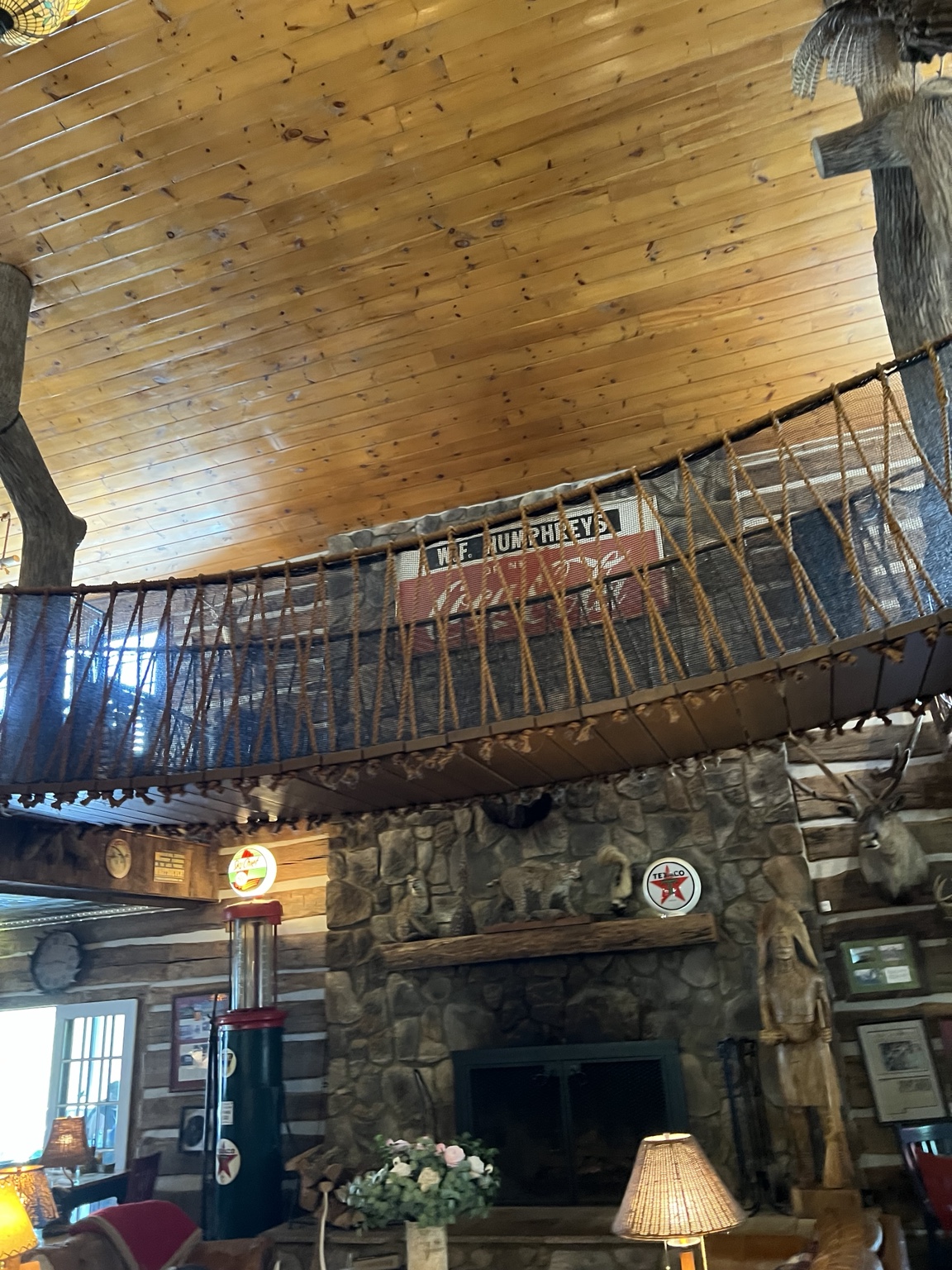 A side view of the indoor rope-and-plank swinging bridge suspended above the Swinging Bridge Restaurant’s stone fireplace