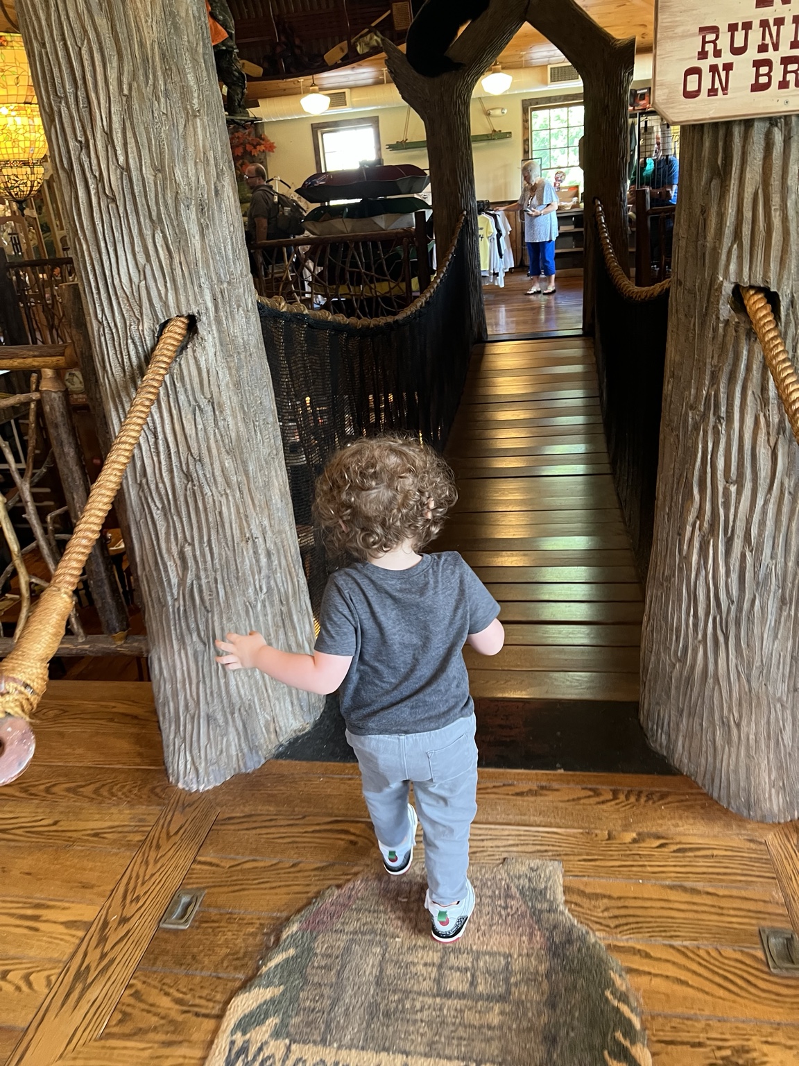 A young child, seen from behind, walking toward the indoor swinging bridge inside the Paint Bank General Store