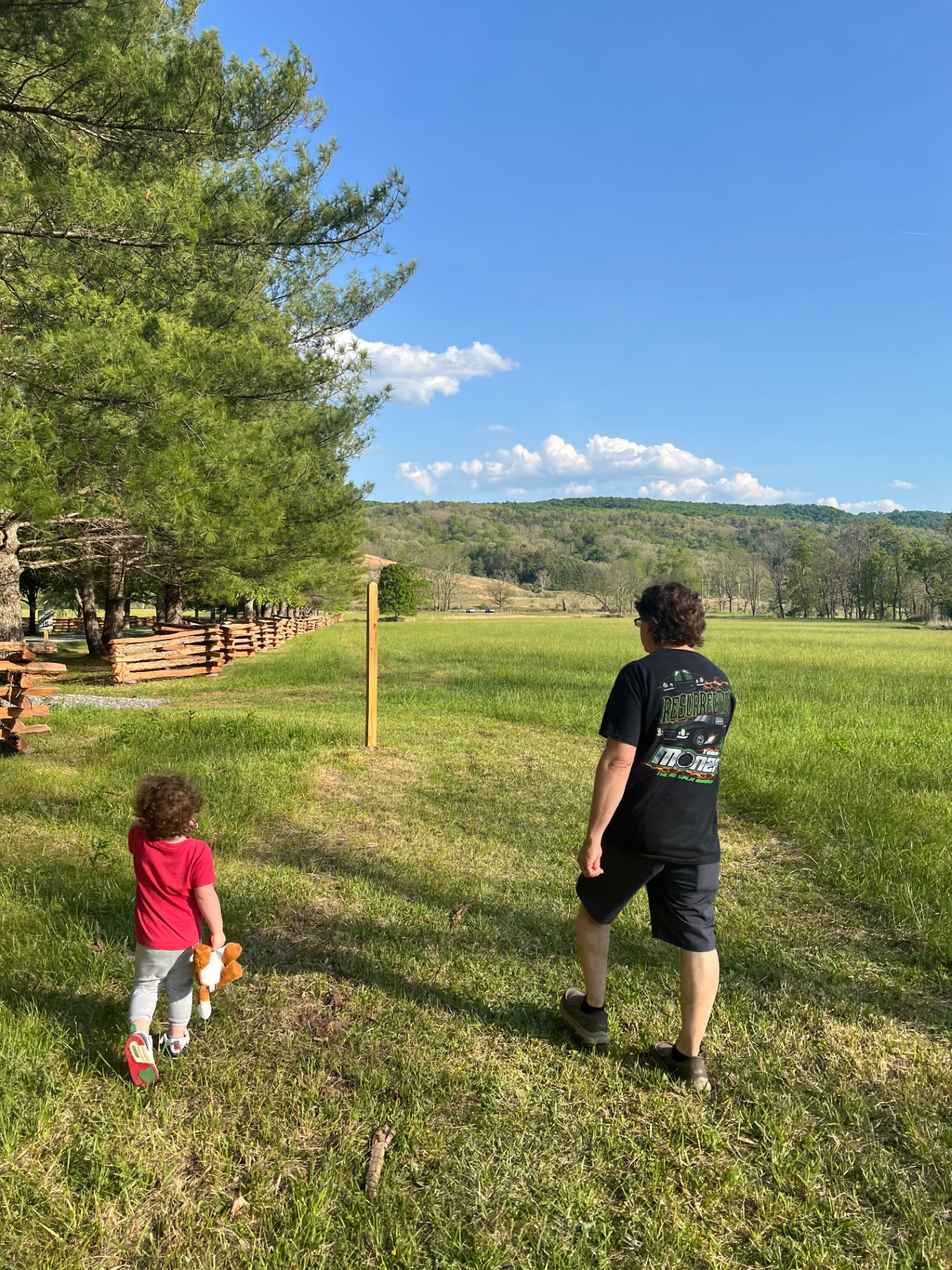A father and young child walk beside a split-rail fence through the open fields on the River Loop Trail.